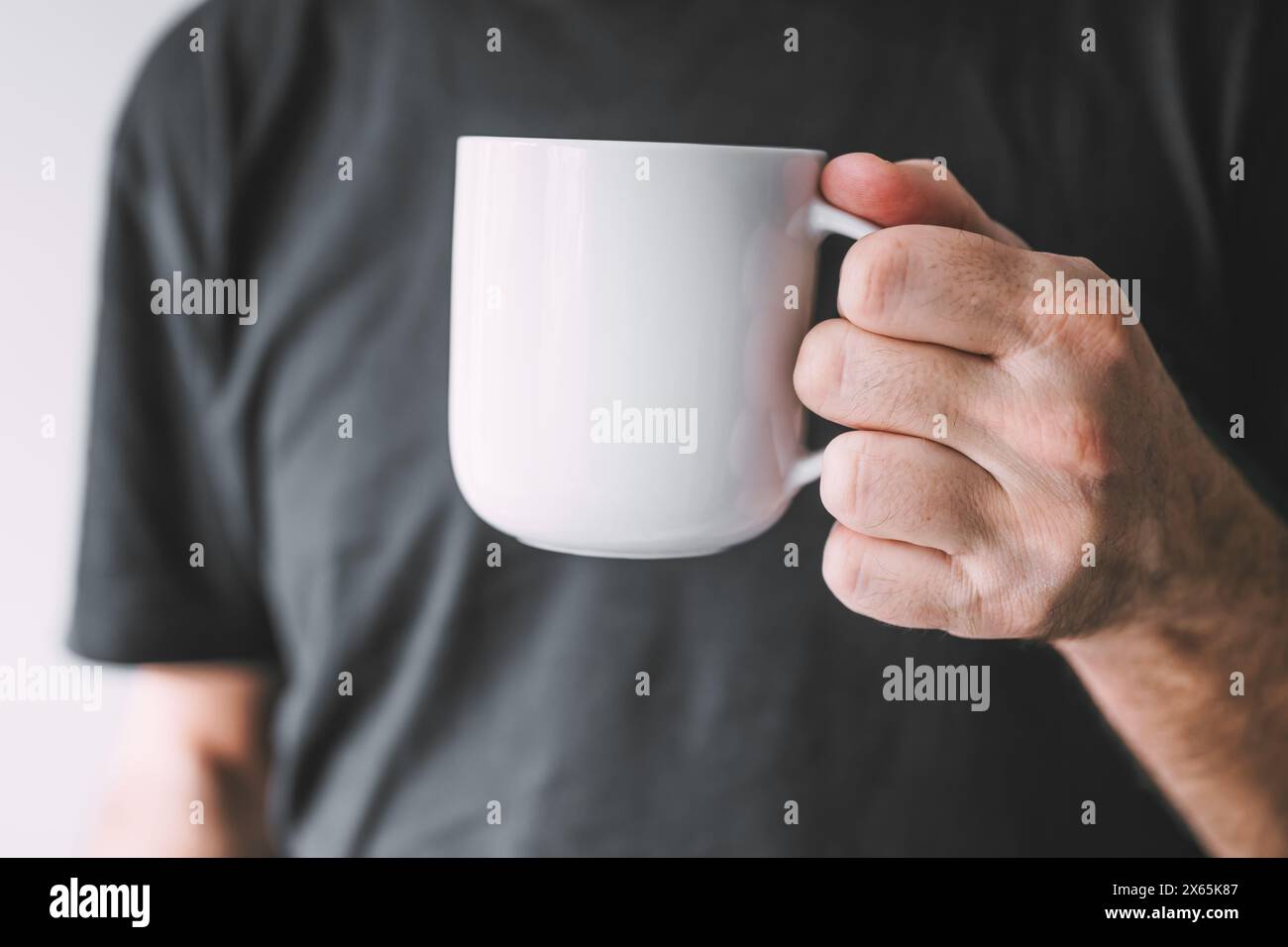 Homme tenant une maquette de tasse à café blanche, mise au point sélective Banque D'Images
