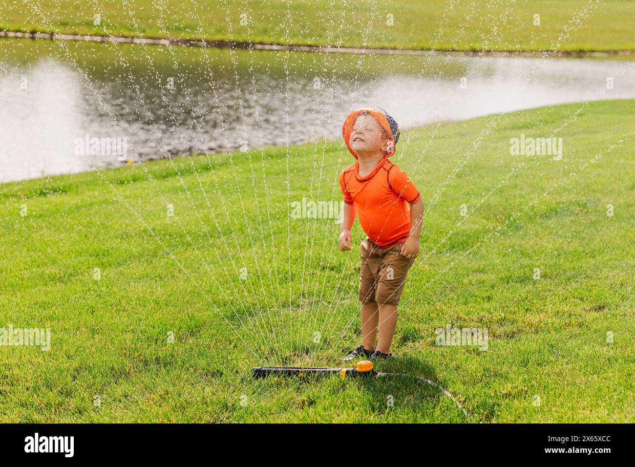 Jeune enfant jouissant de l'eau dans l'arroseur sur l'herbe Banque D'Images