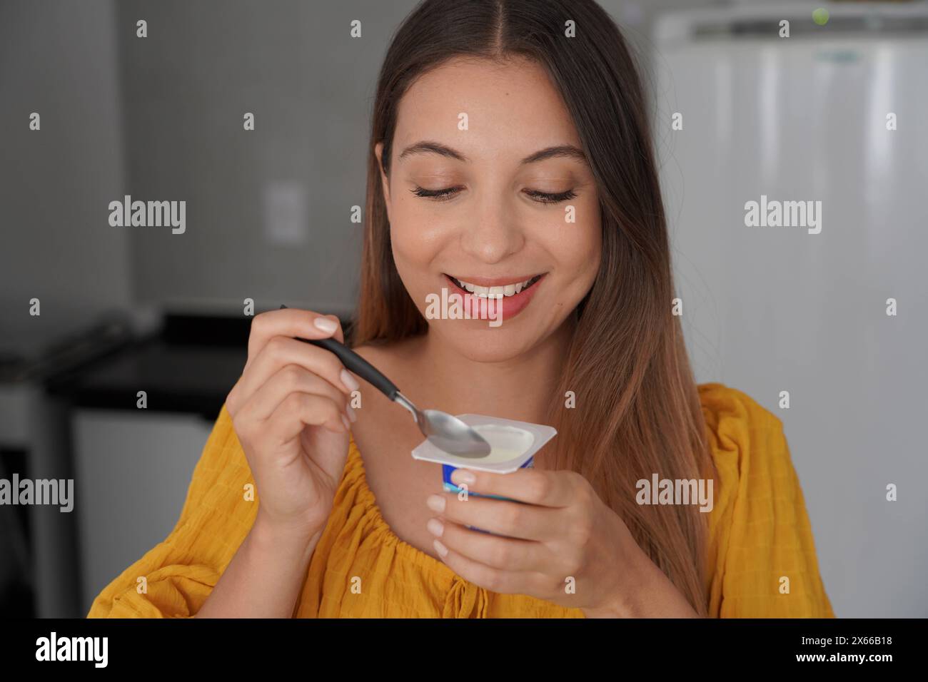 Jeune femme joyeuse hispanique mangeant du yaourt naturel dans la cuisine à la maison Banque D'Images