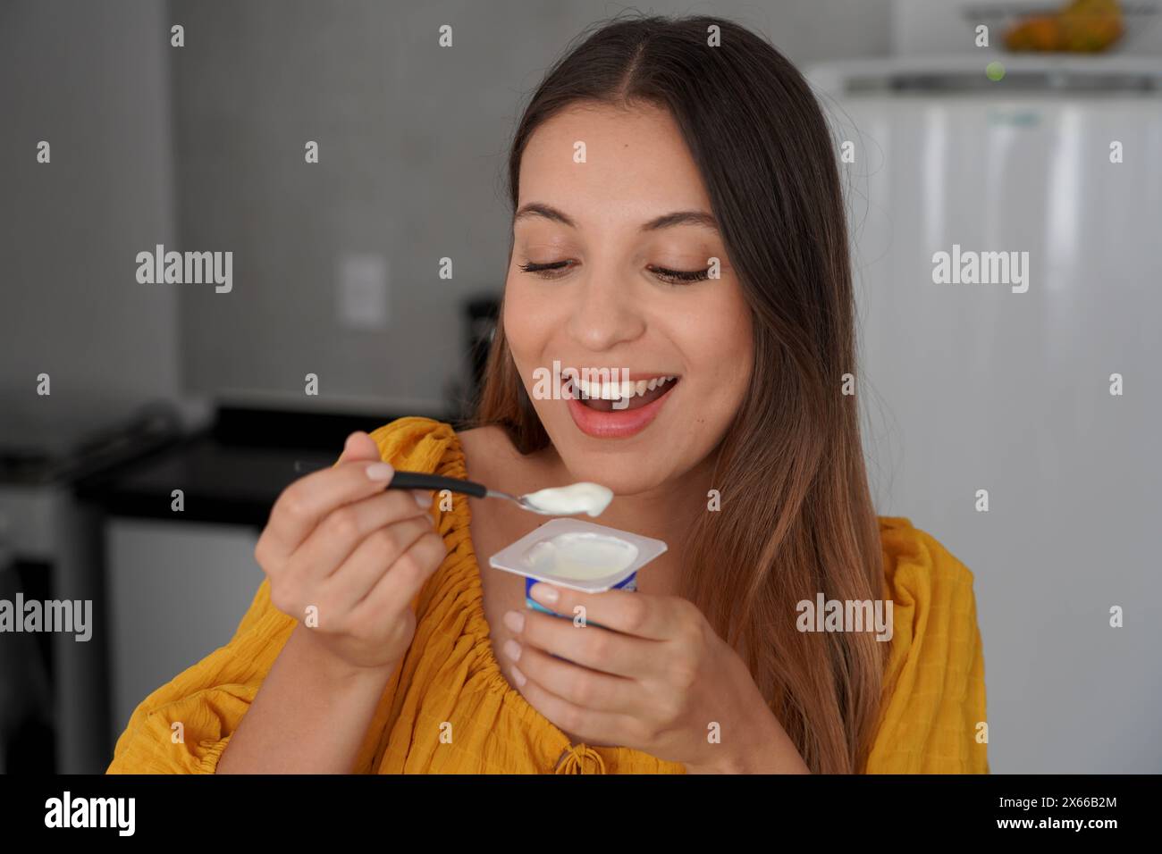 Attrayant jeune femme souriante mangeant du yaourt naturel dans la cuisine à la maison Banque D'Images
