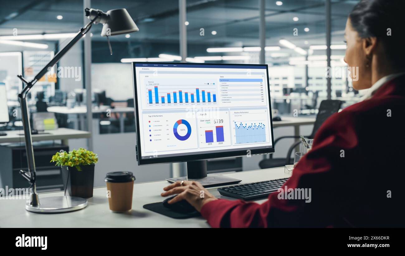 Femme d'affaires réussie assis au bureau travaillant sur ordinateur de bureau dans le bureau de la ville. Top Manager travaillant dur effectuant des recherches pour un projet de commerce électronique avec graphiques, graphiques et tableaux. Au-dessus de l'épaule Banque D'Images