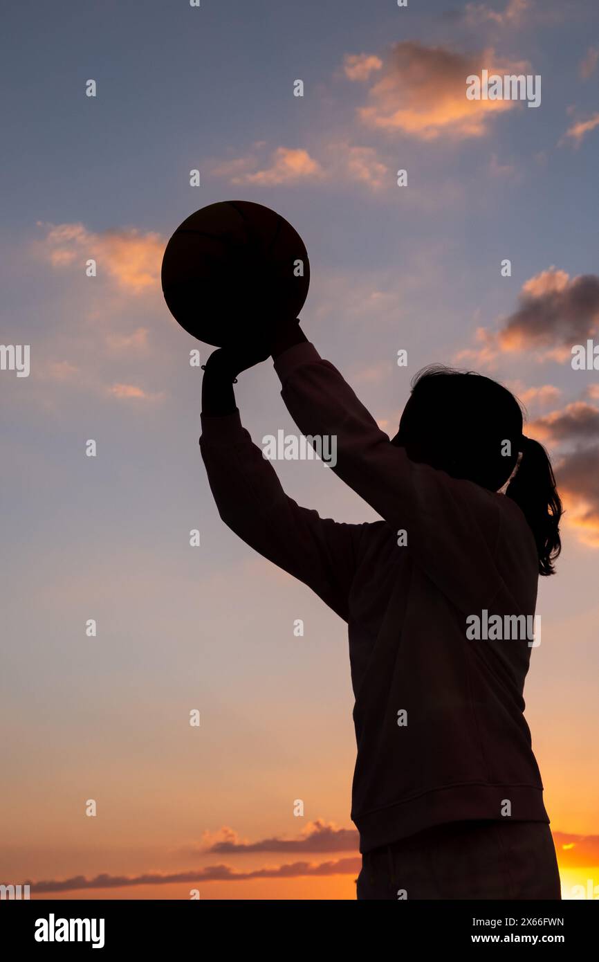 silhouette d'une adolescente tenant une balle de basket-ball dans ses mains au coucher du soleil Banque D'Images