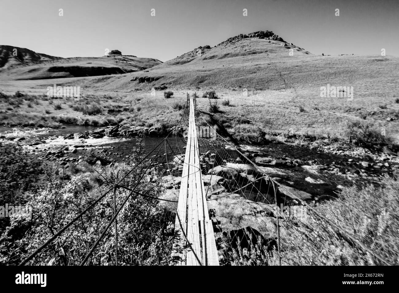 Un pont suspendu traversant la rivière Cobham dans les prairies des montagnes du Drakensberg en Afrique du Sud en noir et blanc Banque D'Images