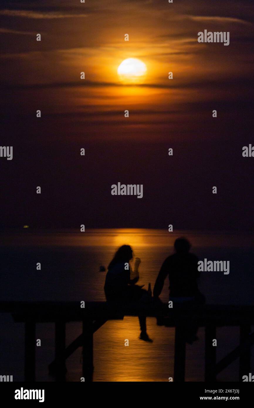 Silhouette de deux personnes sur une passerelle dans la lumière orange de la pleine lune, Dalby, Danemark Banque D'Images