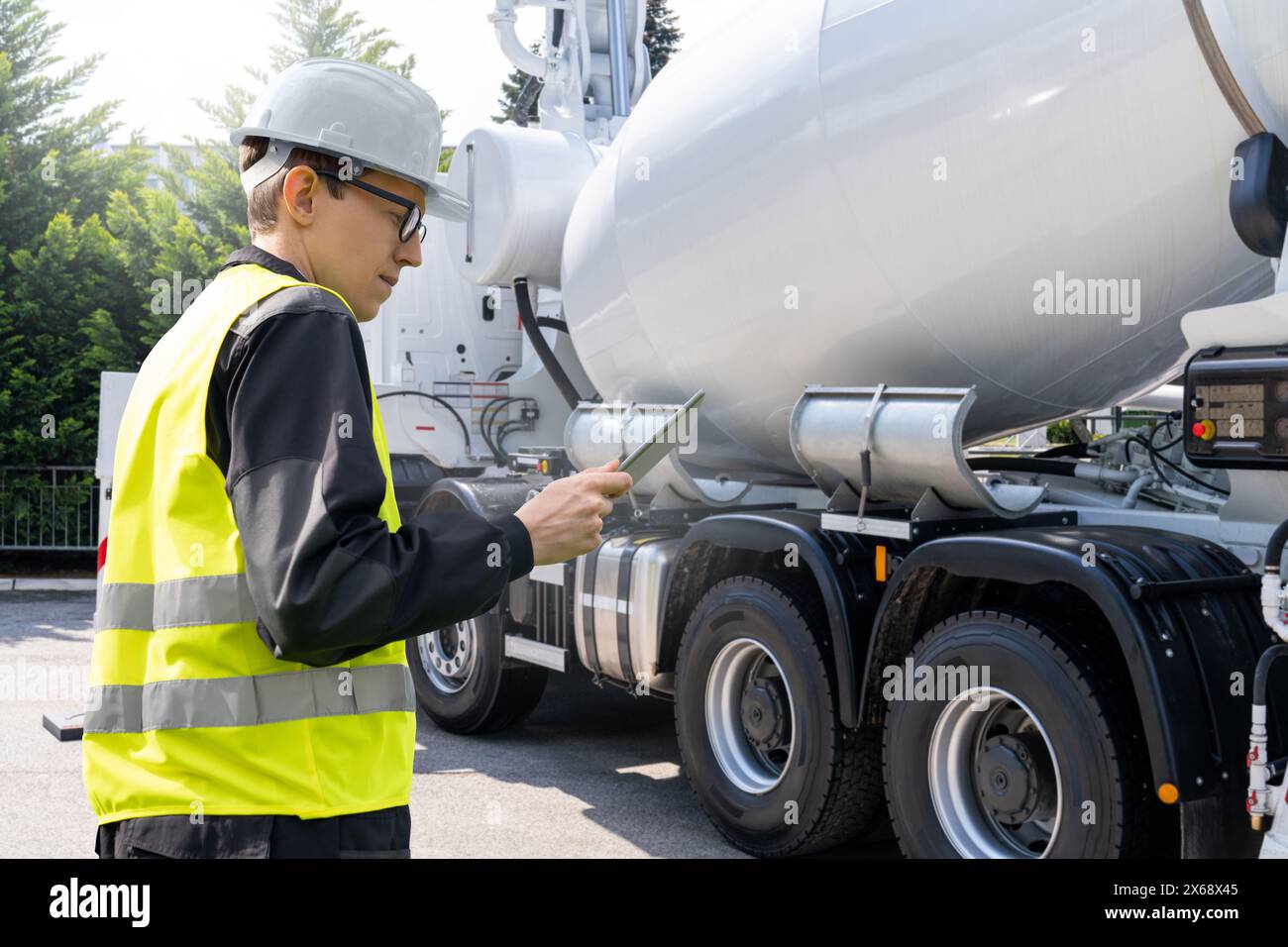 Travailleur avec tablette numérique à côté de la pompe à béton montée sur camion avec mélangeur Banque D'Images