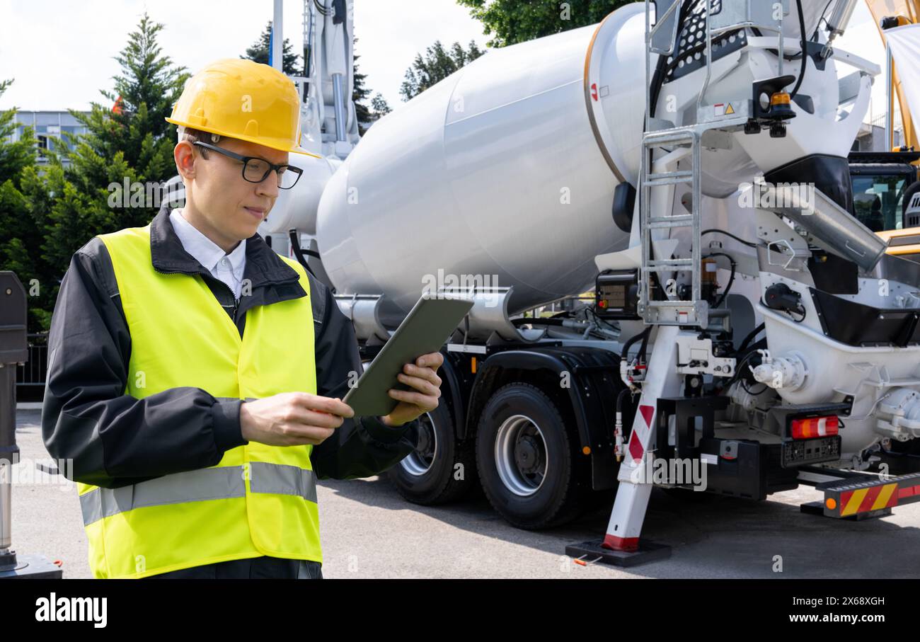 Travailleur avec tablette numérique à côté de la pompe à béton montée sur camion avec mélangeur Banque D'Images