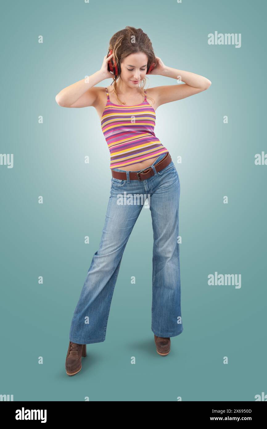 Jeune femme joyeuse qui écoute de la musique à travers des écouteurs, danse et chante tout en étant isolée sur un fond bleu Banque D'Images