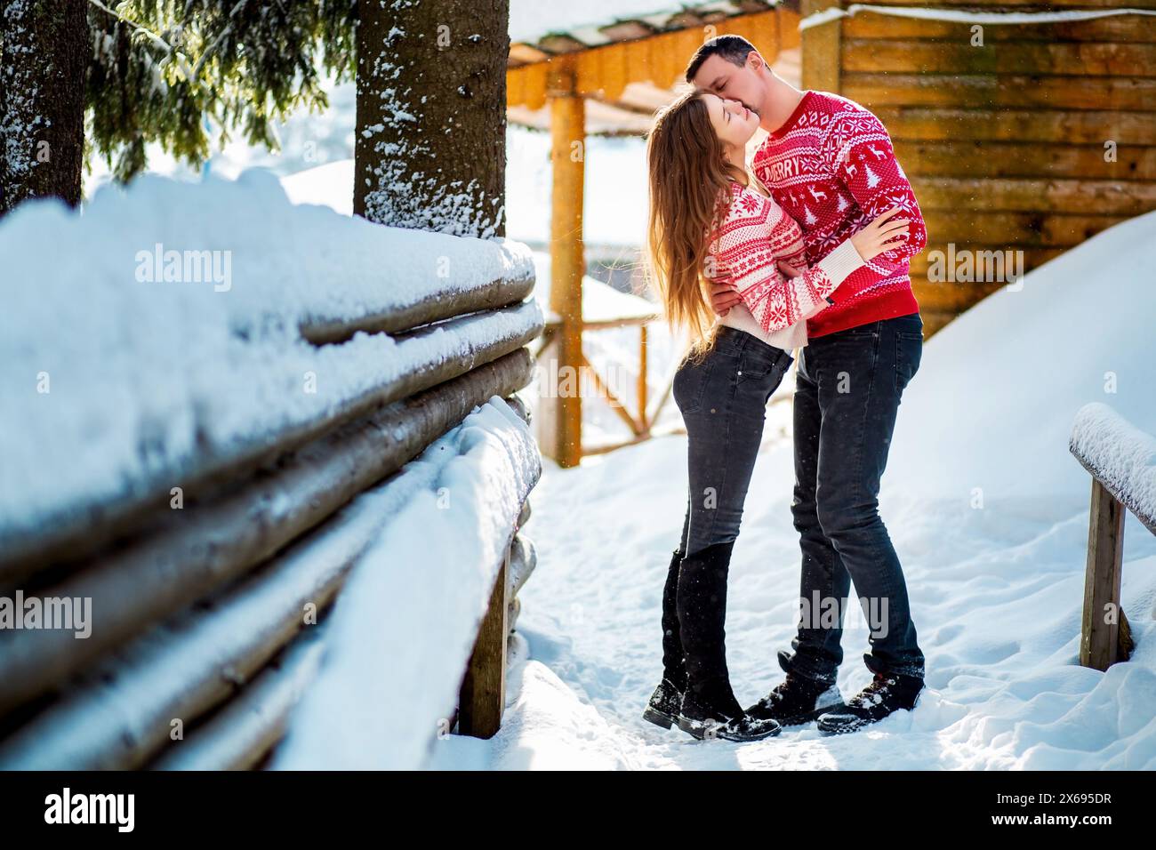 Session de fiançailles, histoire d'amour d'un jeune couple hétéro embrassant et embrassant dans des chandails rouges de Noël et des jeans heureux dans un paysage enneigé près d'un WO Banque D'Images