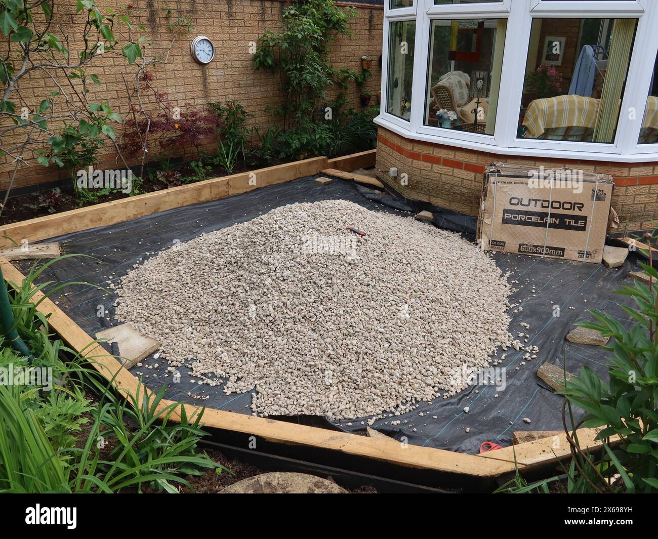 Maquillage du jardin : niveler et compacter le noyau dur, mettre dans la bordure puis poser une membrane avant d'ajouter le gravier pour une terrasse à faible entretien. Banque D'Images