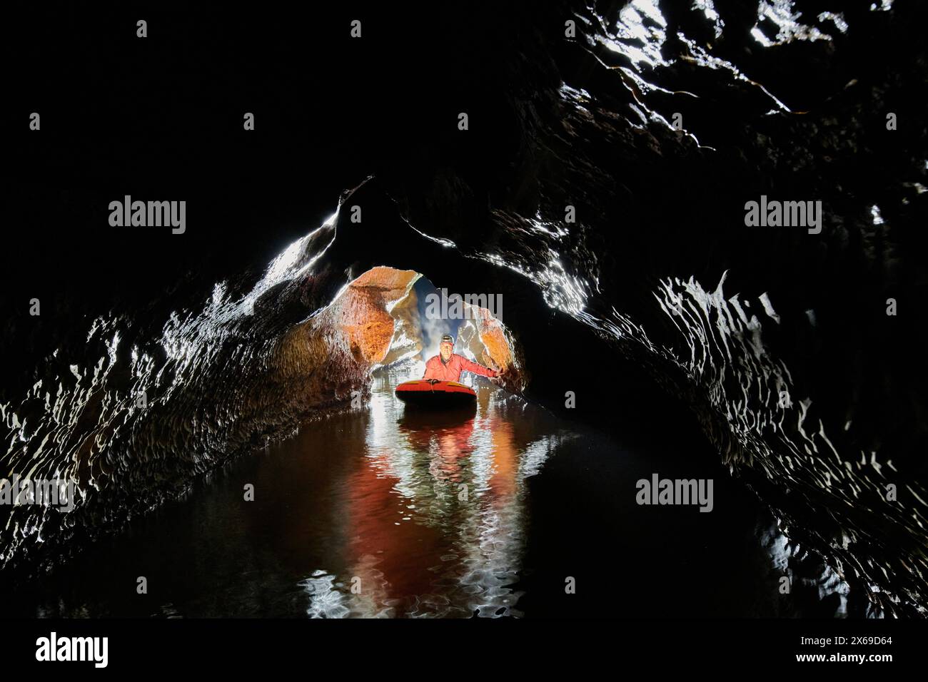 Spéléologue traverse un lac souterrain dans un canot en caoutchouc Banque D'Images