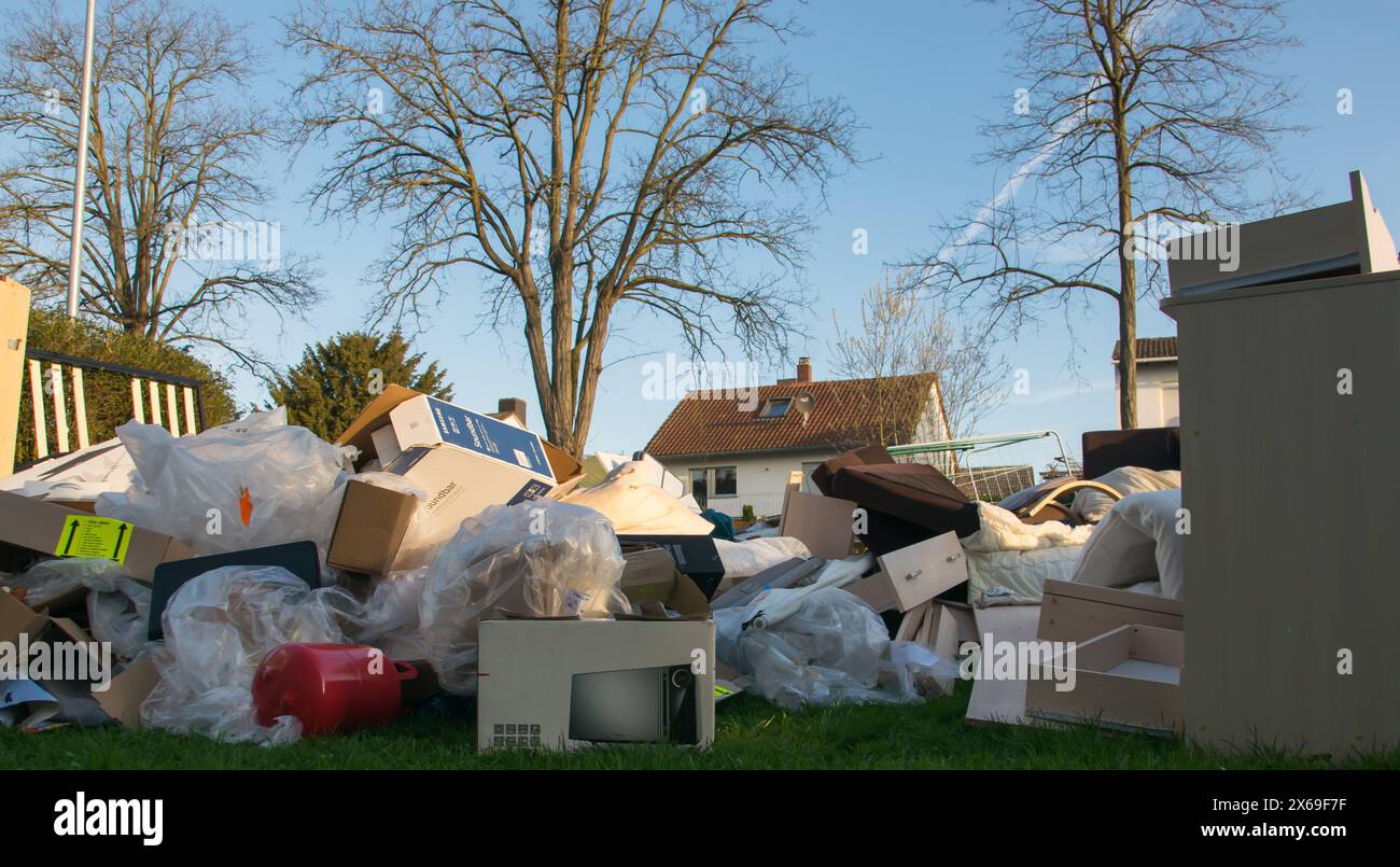 Beaucoup de déchets dans une ville près de la haus. Grandes ordures avec vieux meubles en bois, jouets, boîtes, sacs en plastique dans une rue et l'herbe verte au printemps ensoleillé tra Banque D'Images