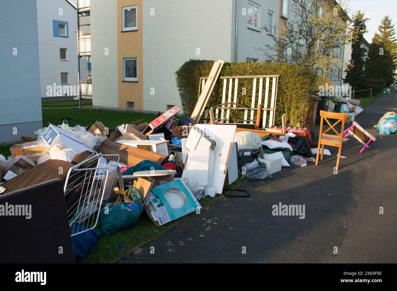 Déchets dans une ville près de la maison. Grandes ordures avec vieux meubles en bois, jouets, boîtes, sacs en plastique dans une rue et l'herbe verte dans la décharge ensoleillée jour après jour Banque D'Images