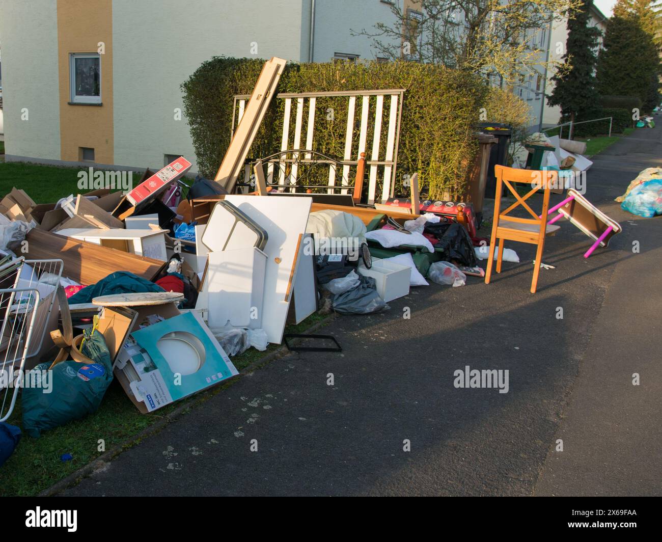 Beaucoup de déchets dans une ville près de la maison. Grandes ordures avec vieux meubles en bois, jouets, boîtes, sacs en plastique dans une rue et herbe verte dans les ordures ensoleillées du printemps Banque D'Images