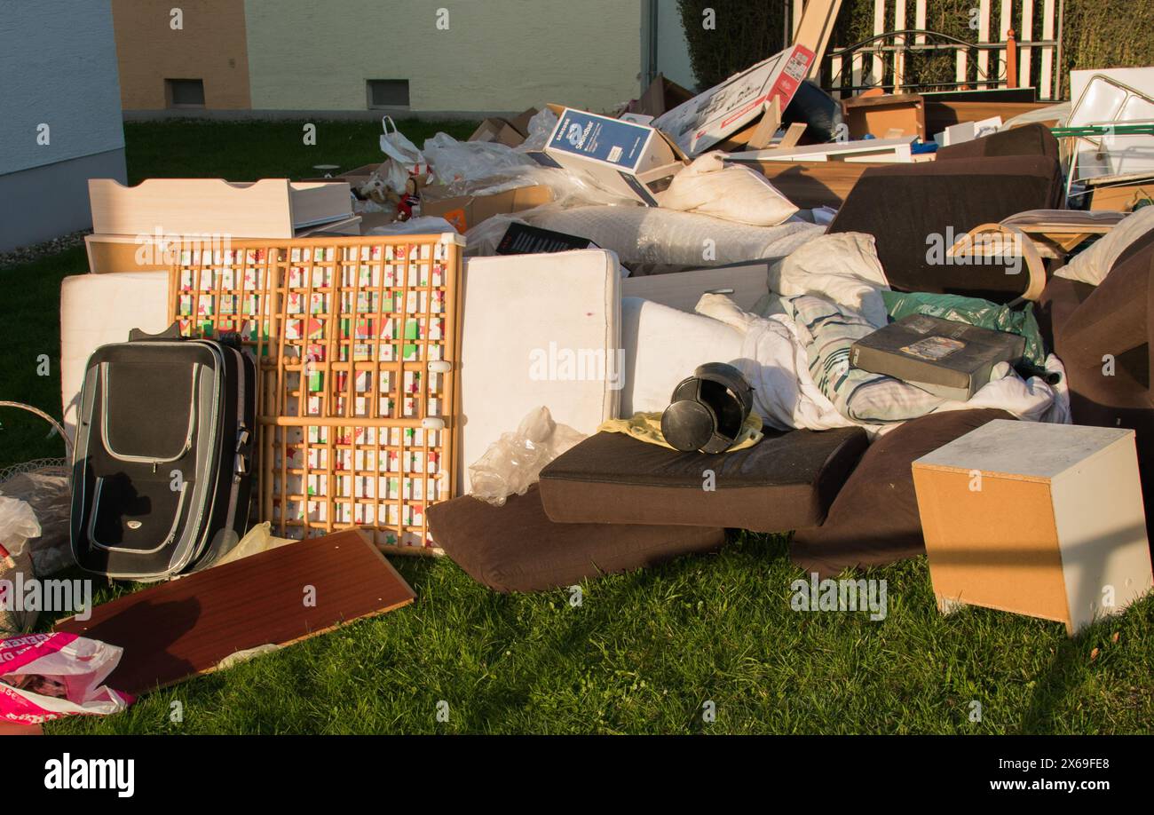 Beaucoup de déchets dans une ville près de la maison. Grandes ordures avec vieux meubles en bois, jouets, boîtes, sacs en plastique dans une rue et l'herbe verte au printemps ensoleillé tr Banque D'Images