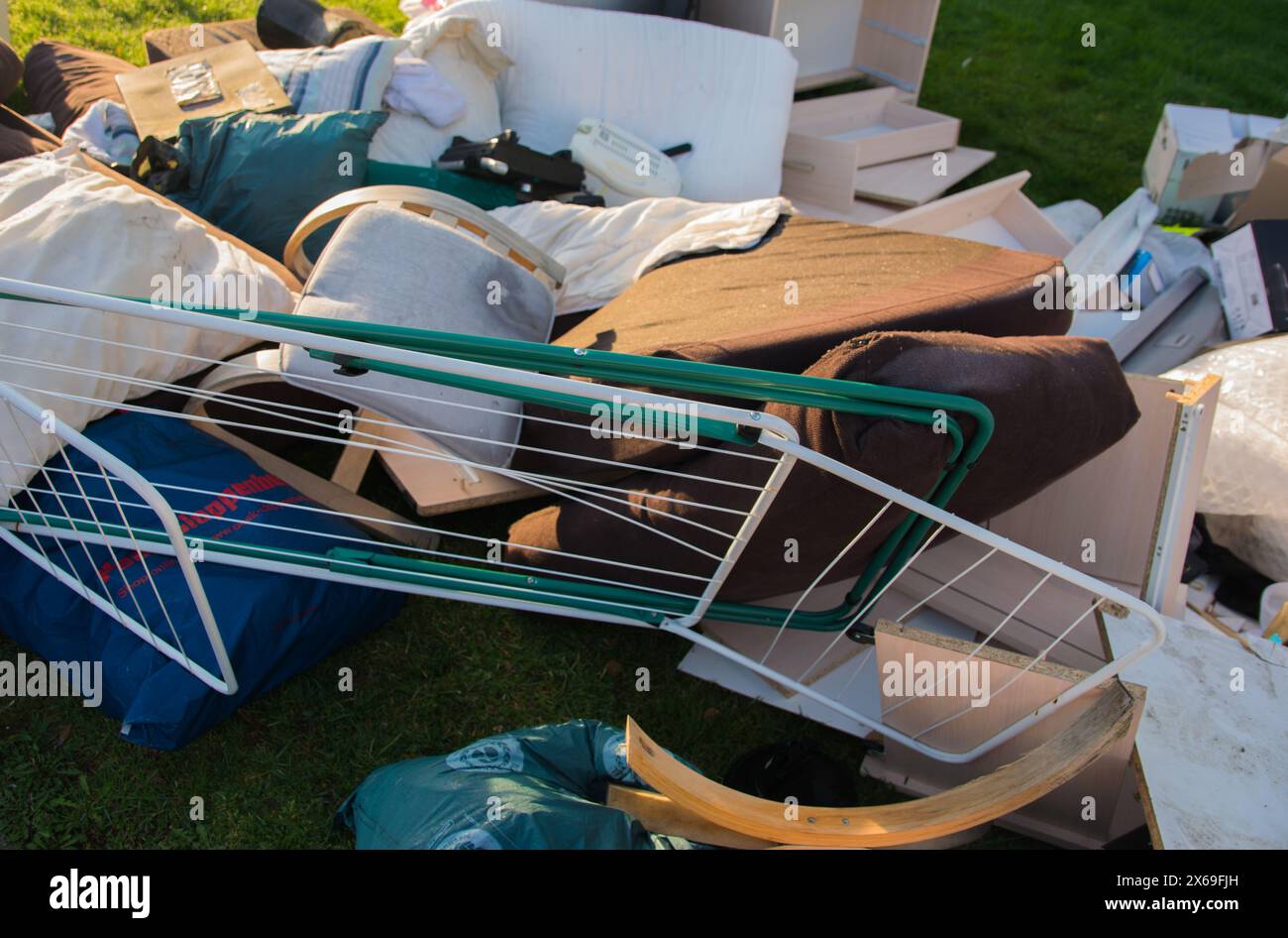 Déchets dans une ville. Grandes ordures avec vieux meubles en bois, jouets, boîtes, sacs en plastique dans une rue et herbe verte au printemps ensoleillé jour de décharge des ordures en Allemagne. Banque D'Images