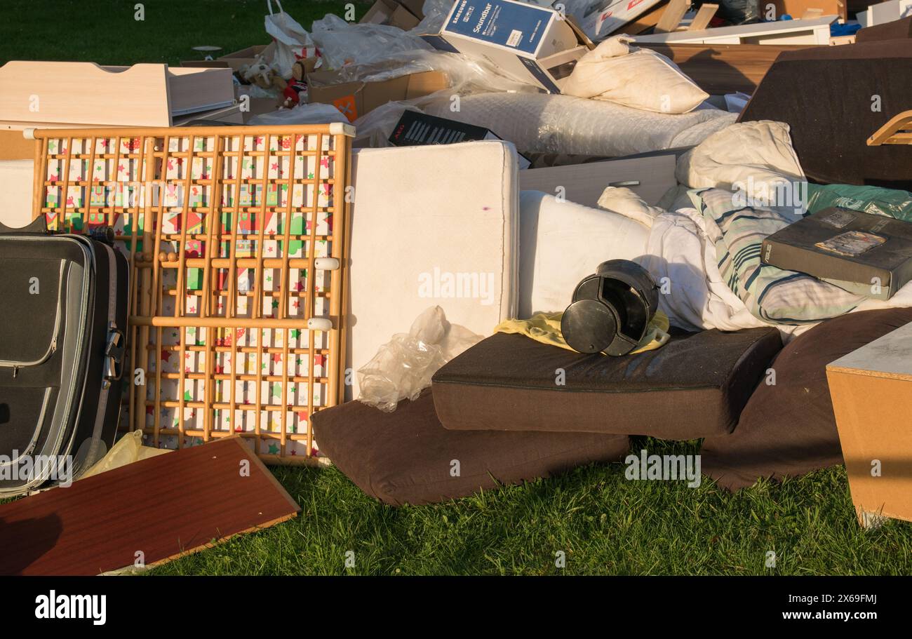 Déchets dans une ville près de la maison. Grandes ordures avec vieux meubles en bois, jouets, boîtes, sacs en plastique dans une rue et l'herbe verte dans la décharge ensoleillée jour après jour Banque D'Images