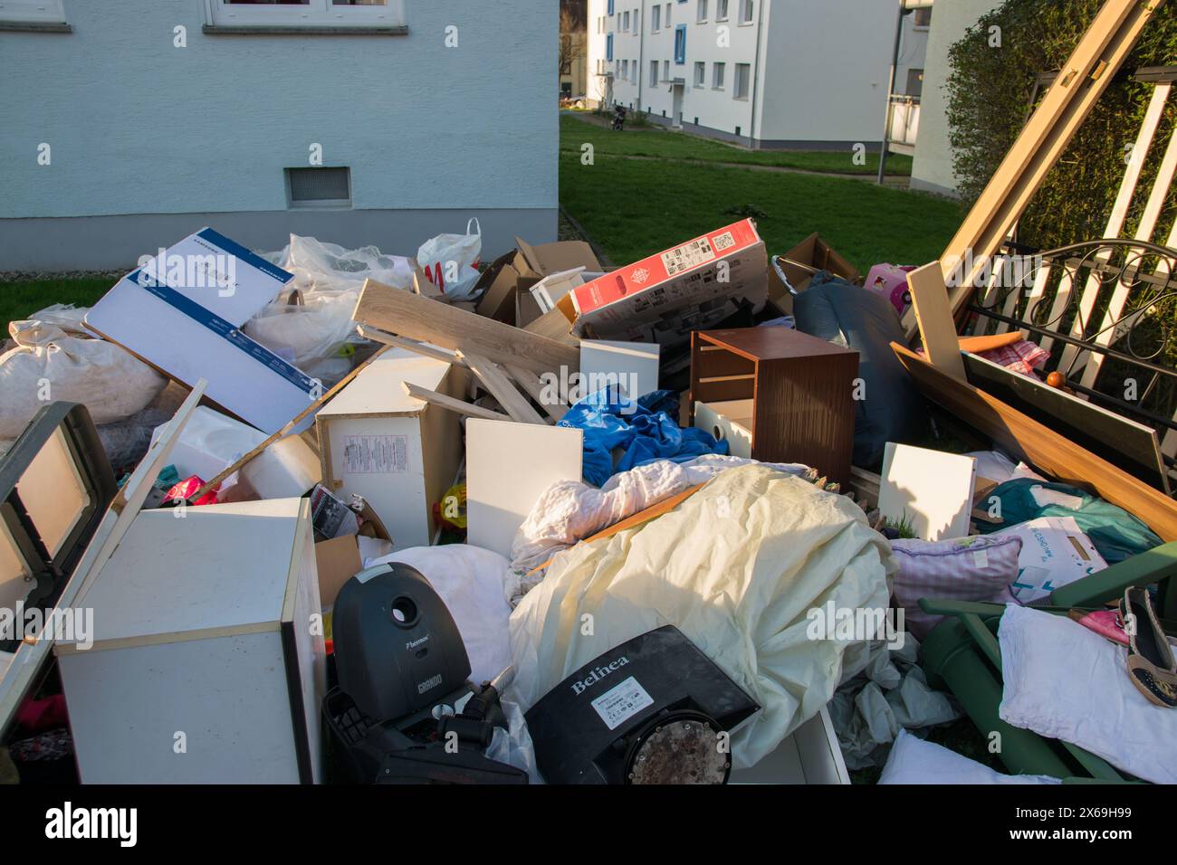 Beaucoup de déchets dans une ville près de la haus. Grandes ordures avec vieux meubles en bois, jouets, boîtes, sacs en plastique dans une rue et l'herbe verte au printemps ensoleillé tra Banque D'Images