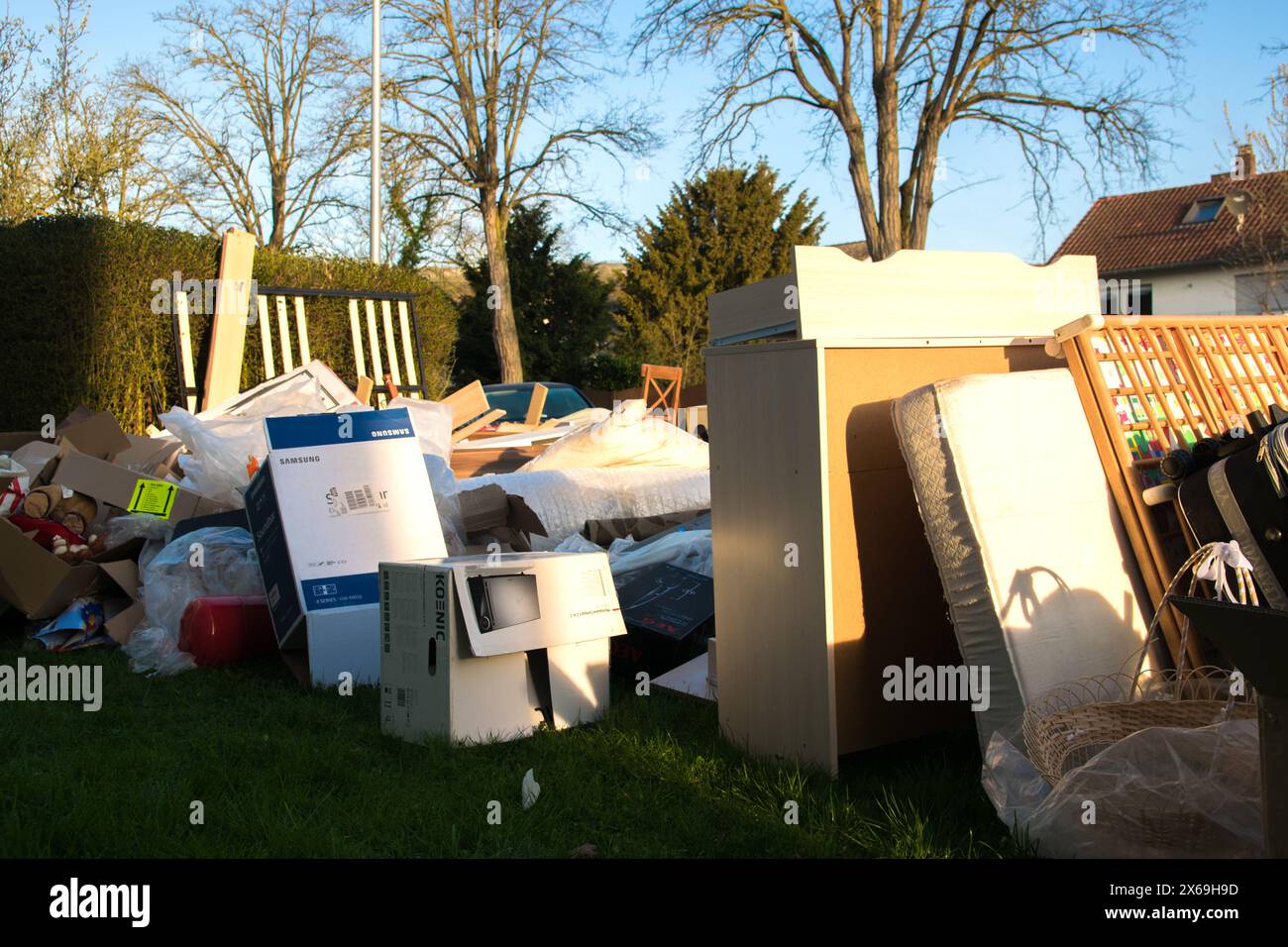 Beaucoup de déchets dans une ville près de la haus. Grandes ordures avec vieux meubles en bois, jouets, boîtes, sacs en plastique dans une rue et l'herbe verte au printemps ensoleillé tra Banque D'Images