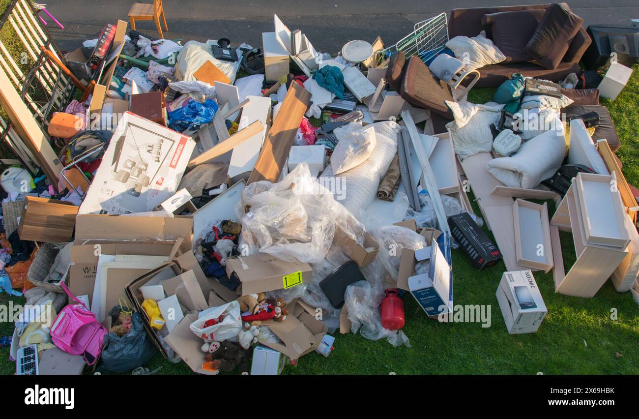 Beaucoup de déchets dans une ville près de la haus. Grandes ordures avec vieux meubles en bois, jouets, boîtes, sacs en plastique dans une rue et l'herbe verte au printemps ensoleillé tra Banque D'Images