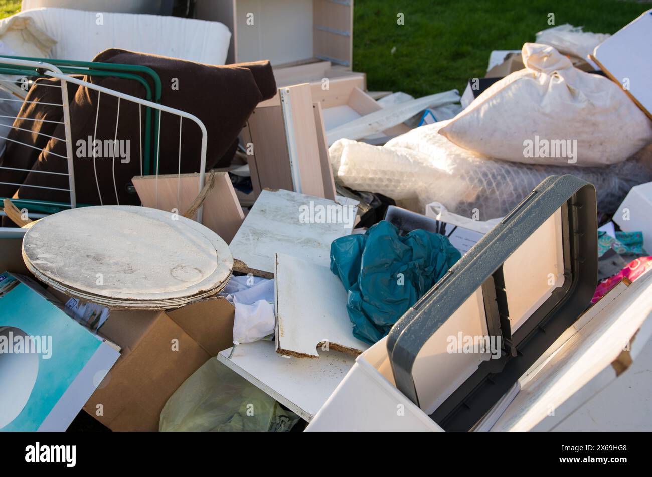 Beaucoup de déchets dans une ville près de la haus. Grandes ordures avec vieux meubles en bois, jouets, boîtes, sacs en plastique dans une rue et l'herbe verte au printemps ensoleillé tra Banque D'Images