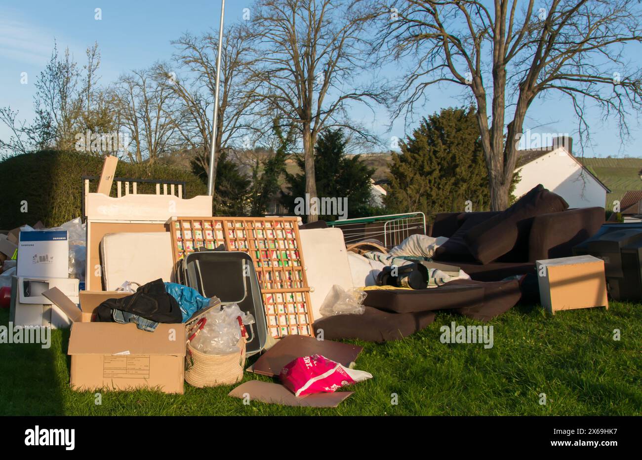 Beaucoup de déchets dans une ville près de la haus. Grandes ordures avec vieux meubles en bois, jouets, boîtes, sacs en plastique dans une rue et l'herbe verte au printemps ensoleillé tra Banque D'Images
