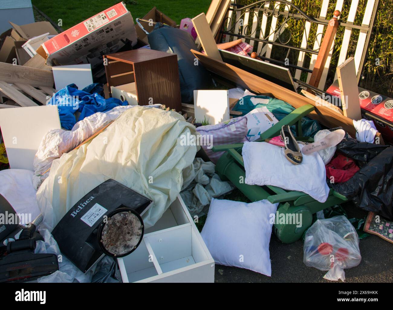 Déchets dans une ville près de la haus. Grandes ordures avec vieux meubles en bois, jouets, boîtes, sacs en plastique dans une rue et l'herbe verte au printemps ensoleillé décharge de déchets d Banque D'Images