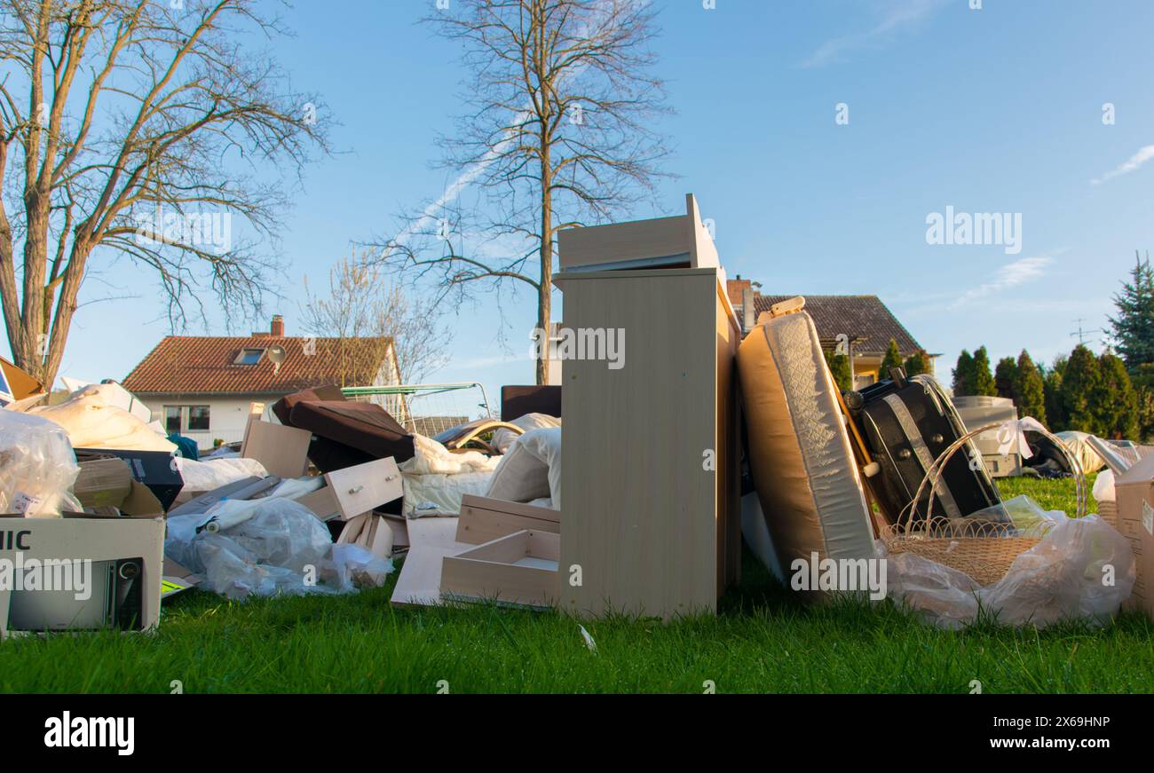Beaucoup de déchets dans une ville près de la haus. Grandes ordures avec vieux meubles en bois, jouets, boîtes, sacs en plastique dans une rue et l'herbe verte au printemps ensoleillé tra Banque D'Images
