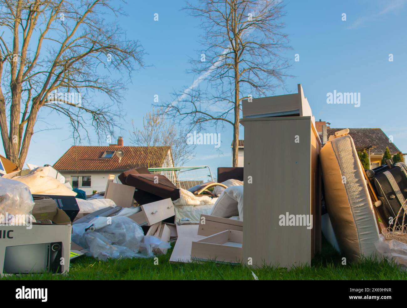 Déchets dans une ville près de la haus. Grandes ordures avec vieux meubles en bois, jouets, boîtes, sacs en plastique dans une rue et l'herbe verte au printemps ensoleillé décharge de déchets d Banque D'Images