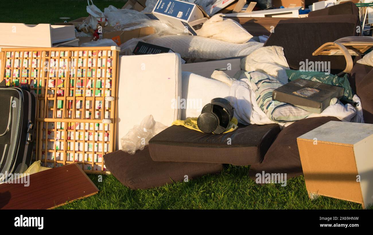 Grandes ordures avec vieux meubles en bois, jouets, boîtes, sacs en plastique dans une rue et herbe verte au printemps ensoleillé jour de décharge des ordures en Allemagne. Déchets dans une ville Banque D'Images