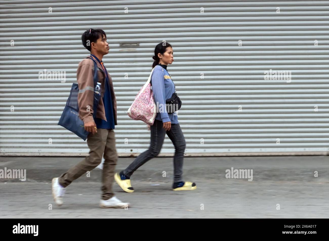 SAMUT PRAKAN, THAÏLANDE, 16 mars 2024, Un couple descend le trottoir à côté d'un mur métallique Banque D'Images