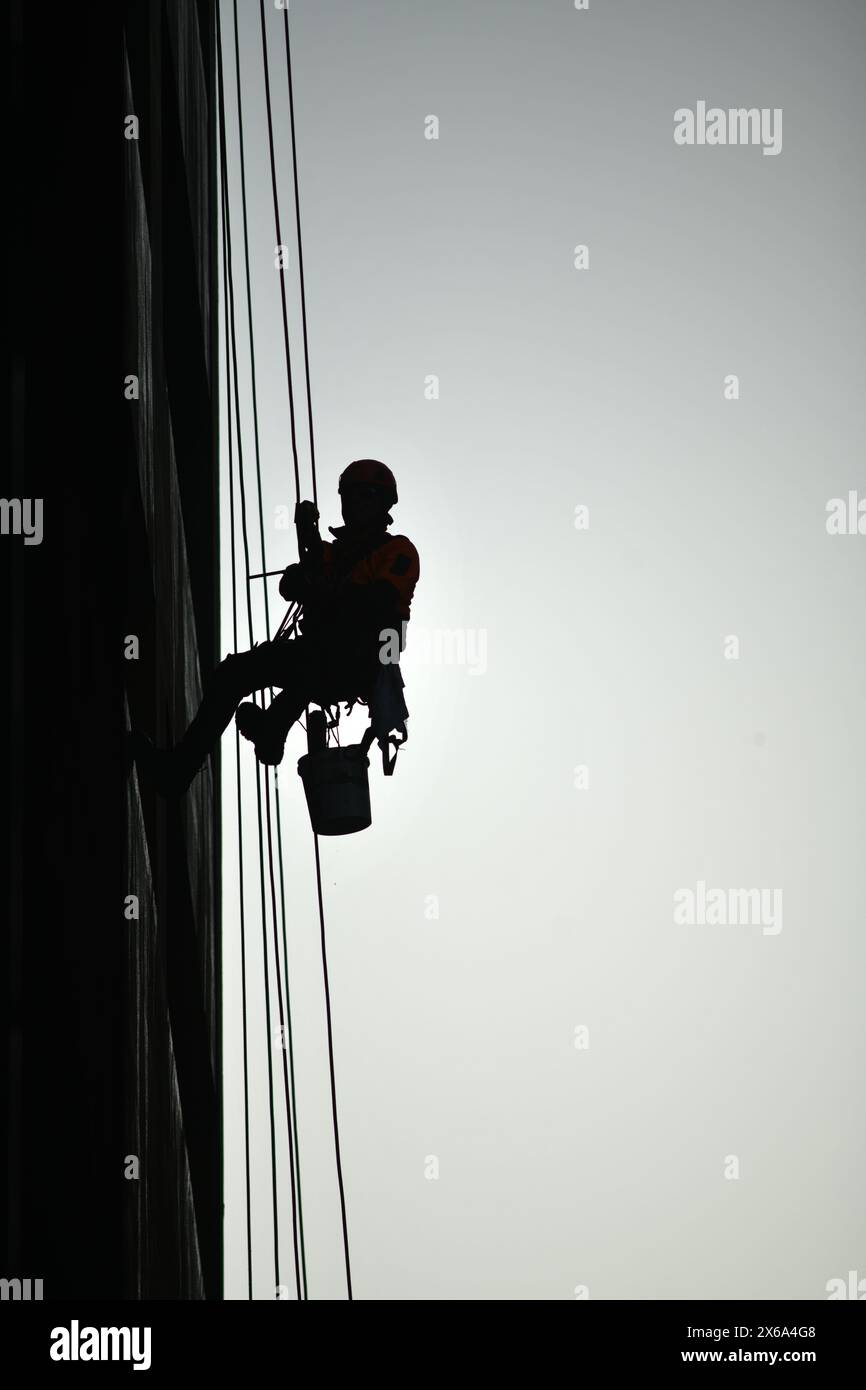 Silhouette d'un homme descendant en rappel et lavant les fenêtres sur un immeuble de grande hauteur Banque D'Images