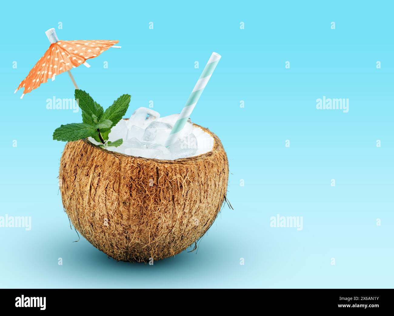 Cocktail exotique servi dans une coquille de coco garnie de menthe, paille à boire et pic de parapluie cocktail sur fond bleu avec espace pour le texte. Banque D'Images