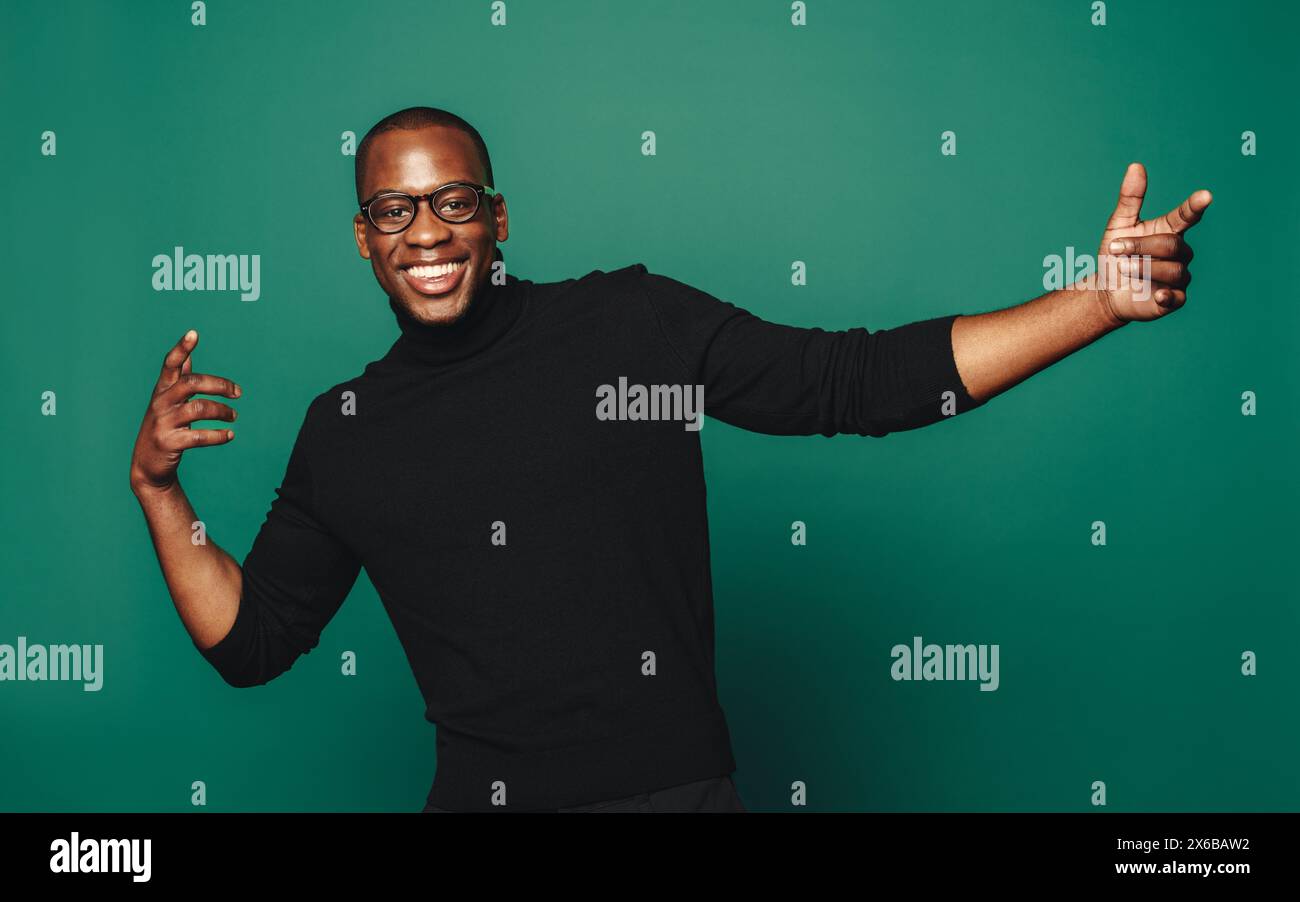 Jeune homme confiant et insouciant dans des vêtements décontractés à la mode, souriant et posant avec des lunettes élégantes. Le fond vert accentue son bonheur et sa mode Banque D'Images