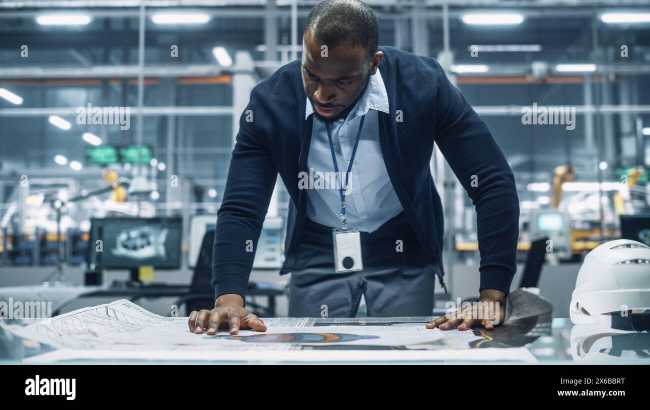 Ingénieur afro-américain examinant un plan technique au travail dans un bureau à l'usine de montage de voitures. Spécialiste industriel travaillant sur les pièces de véhicules dans l'installation de développement technologique. Banque D'Images
