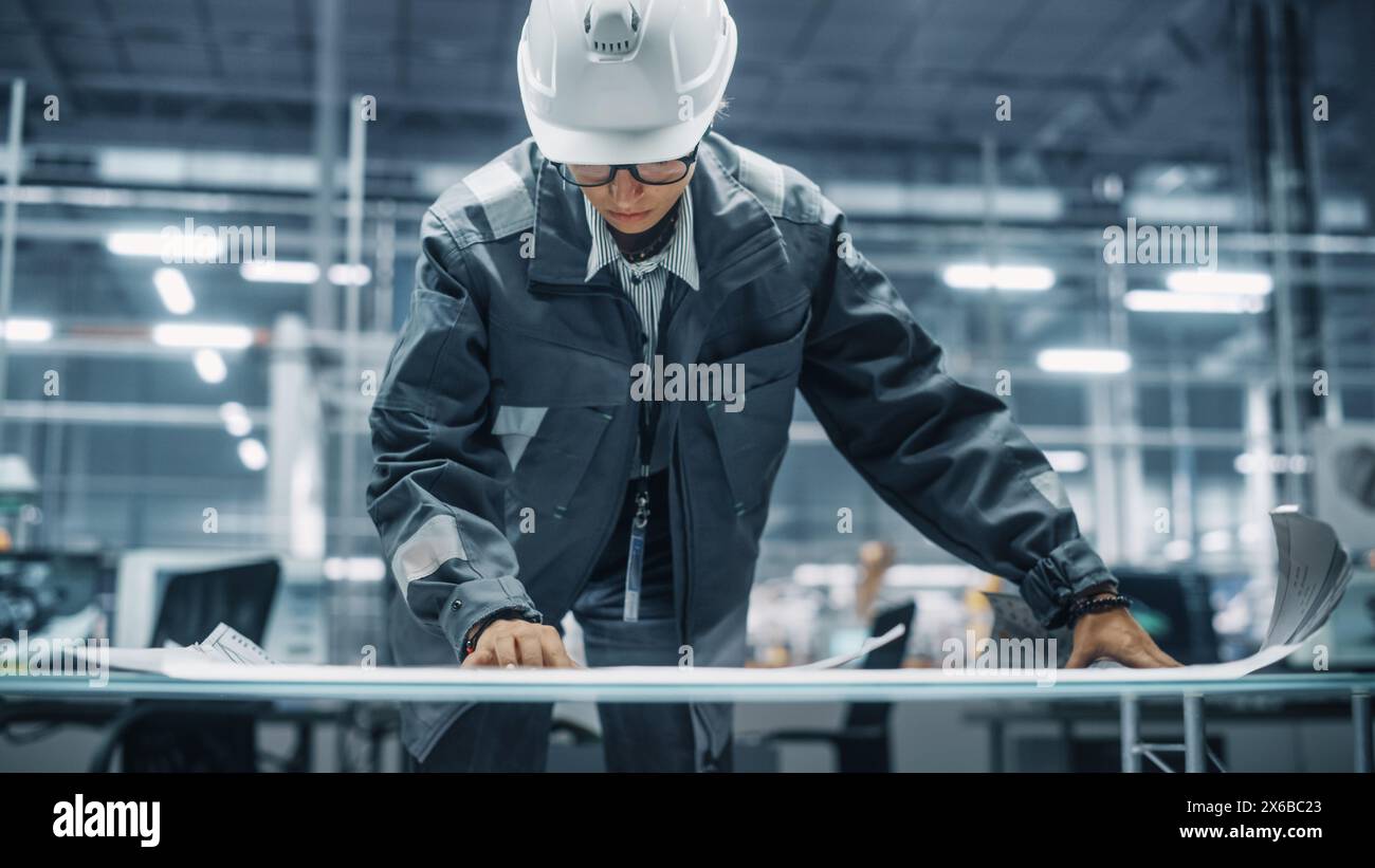 Jeune femme ingénieur en uniforme regardant un plan technique au travail dans un bureau à l'usine d'assemblage de voitures. Spécialiste industriel travaillant sur les pièces de véhicules dans l'installation de développement technologique. Banque D'Images