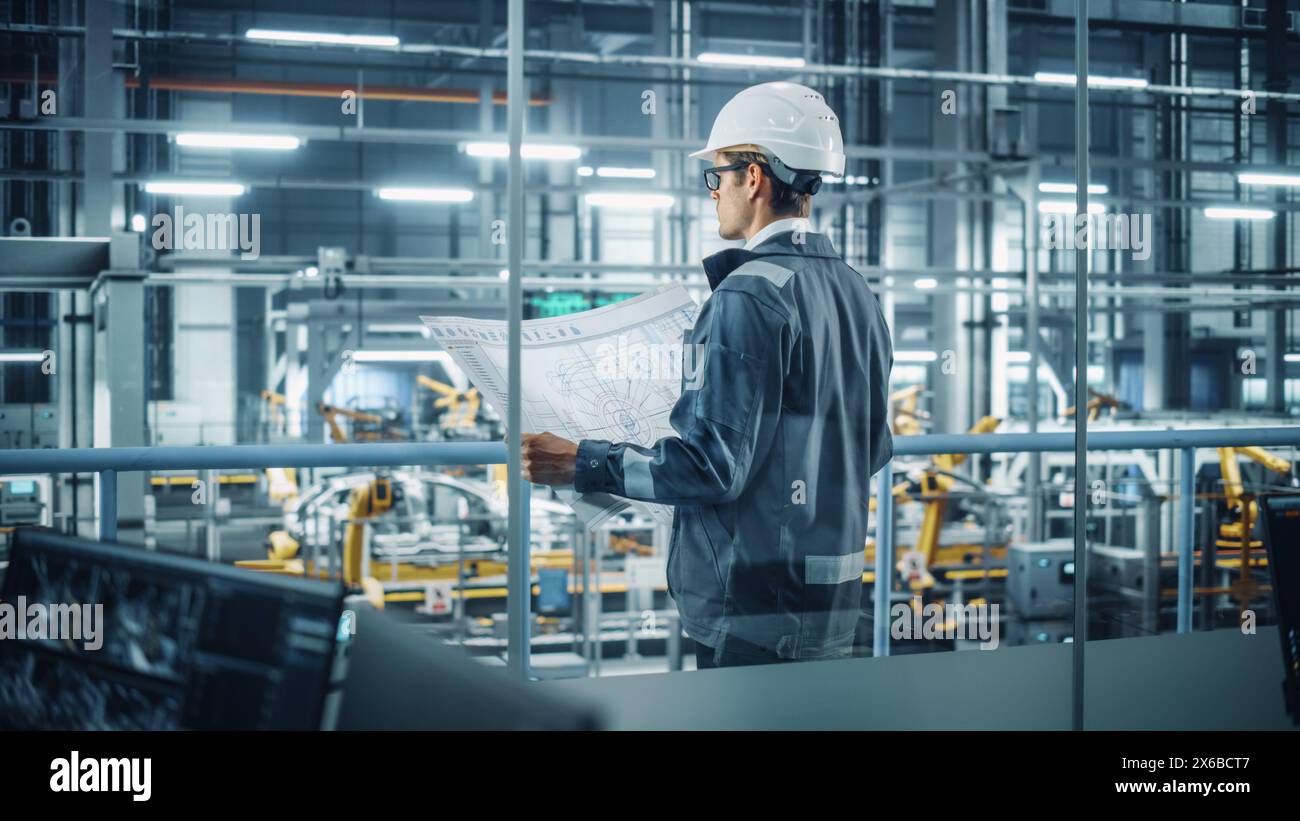Ingénieur en uniforme et casque de sécurité examinant un plan technique au travail dans un bureau à l'usine de montage de voitures. Spécialiste industriel travaillant sur les pièces de véhicules dans l'installation de développement technologique. Banque D'Images
