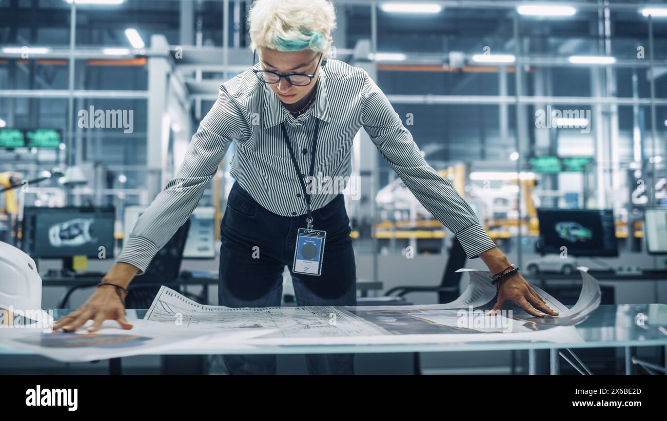 Jeune ingénieur féminin regardant un plan technique au travail dans un bureau à l'usine de montage de voitures. Spécialiste industriel travaillant sur les pièces de véhicules dans l'installation de développement technologique. Banque D'Images
