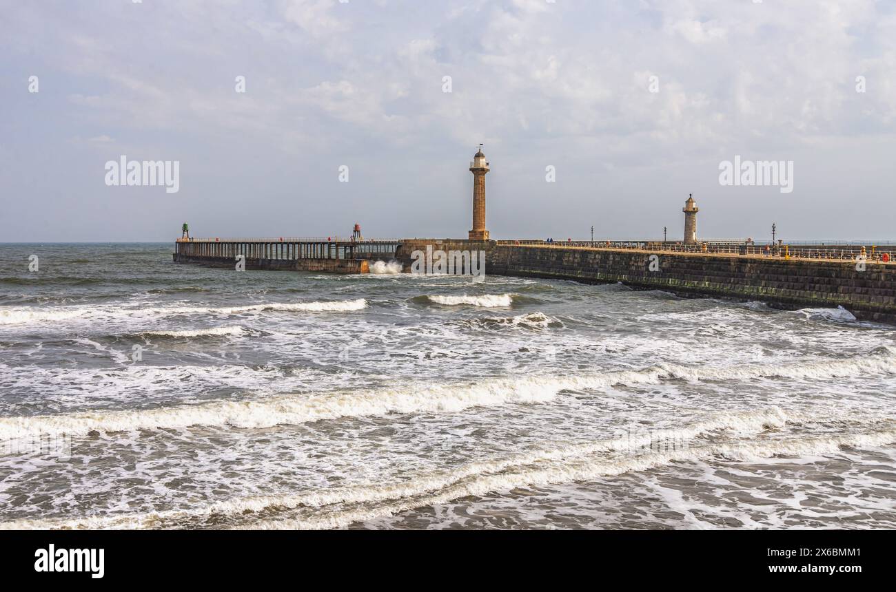 Une jetée avec un phare s'étend dans une mer orageuse tandis que les vagues avec de l'mousse blanche rugissent sur le rivage. Un deuxième phare est au-delà. Banque D'Images