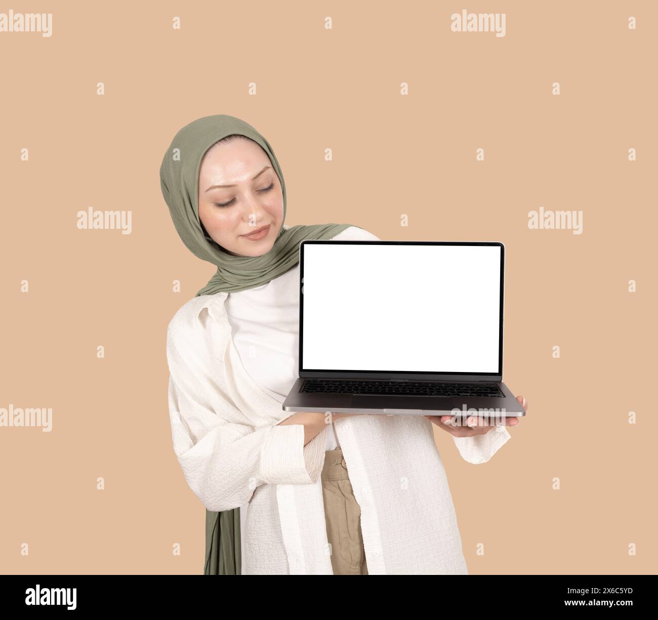 Jeune femme musulmane en hijab tenant une maquette d'ordinateur portable. Fille caucasienne portant un foulard de tête regardant l'écran vide blanc blanc du cahier moderne. Banque D'Images