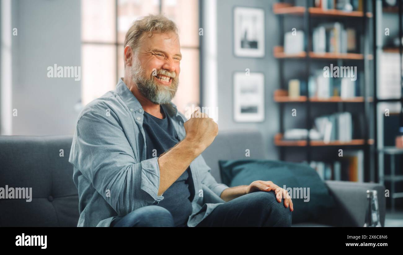 Charismatique homme barbu assis sur un canapé regarde le jeu à la télévision, célèbre le sport quand l'équipe gagne le championnat. Concentré, joyeusement intense et auteure de fan quand le club préféré joue Banque D'Images