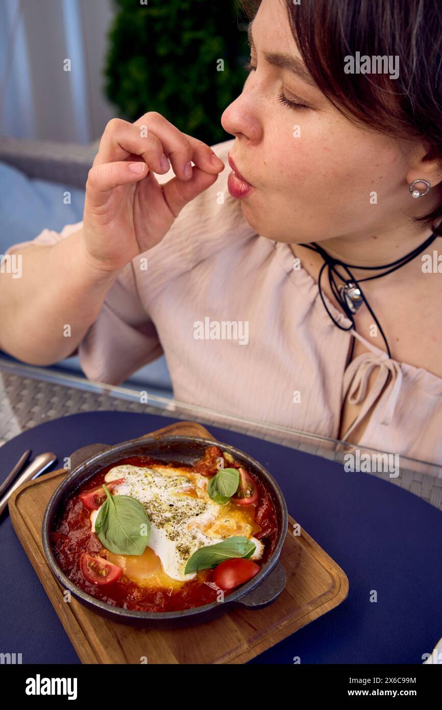 Une femme de taille moyenne en robe fuzz pêche mangeant Shakshouka dans un restaurant moderne Banque D'Images