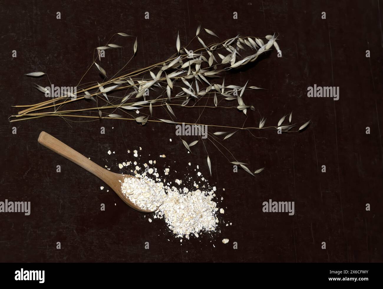 Une branche de farine d'avoine séchée à côté d'une cuillère avec ses graines, vue d'en haut, photo studio isolée sur fond de bois Banque D'Images