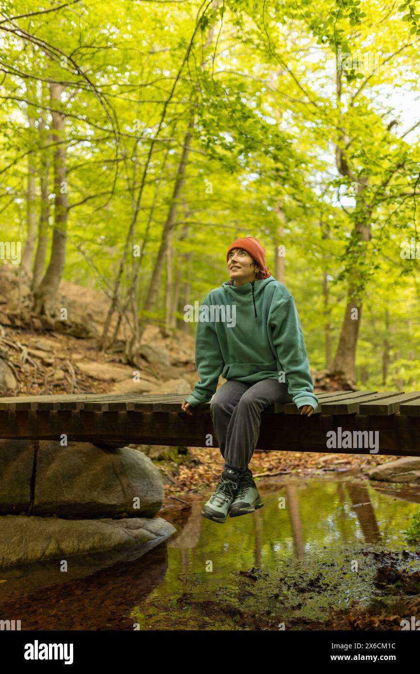 femme dans la forêt assise sur un pont avec chapeau orange chapeau, sur un voyage à la recherche de nouveau à découvrir, levant les yeux Banque D'Images