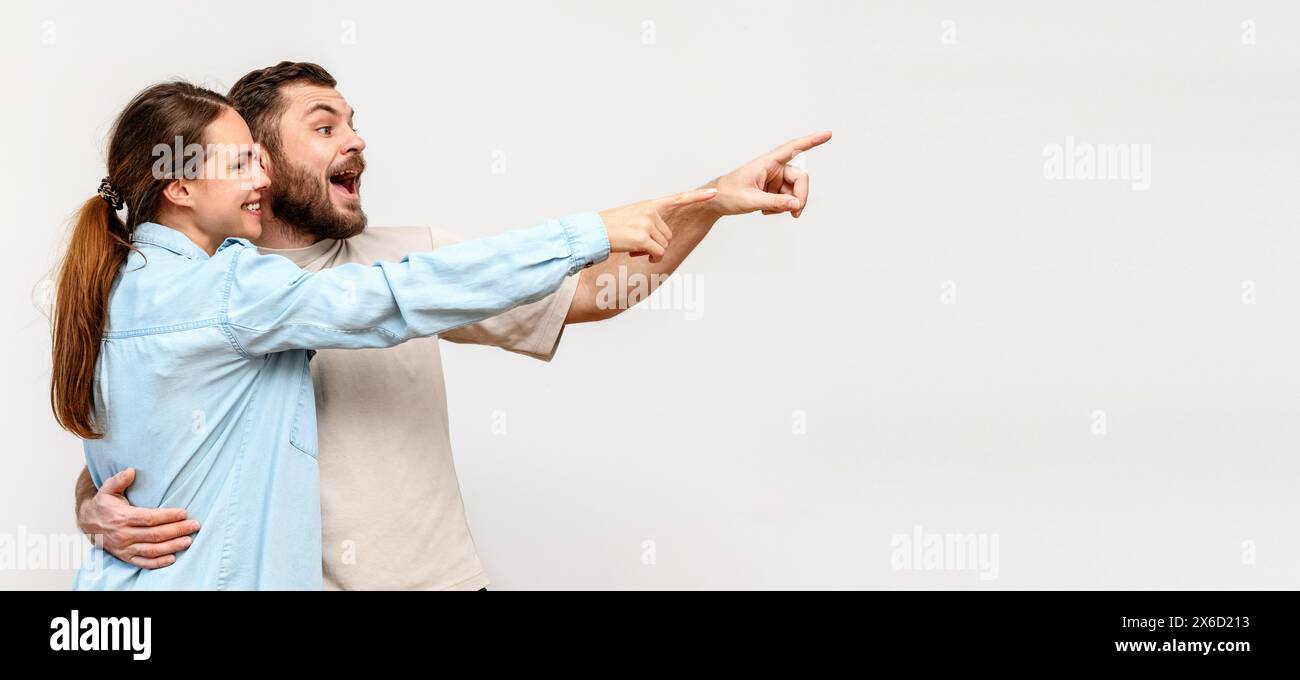 Couple heureux et surpris pointant du doigt l'objet virtuel. Bannière publicitaire et marketing avec des consommateurs satisfaits. Banque D'Images