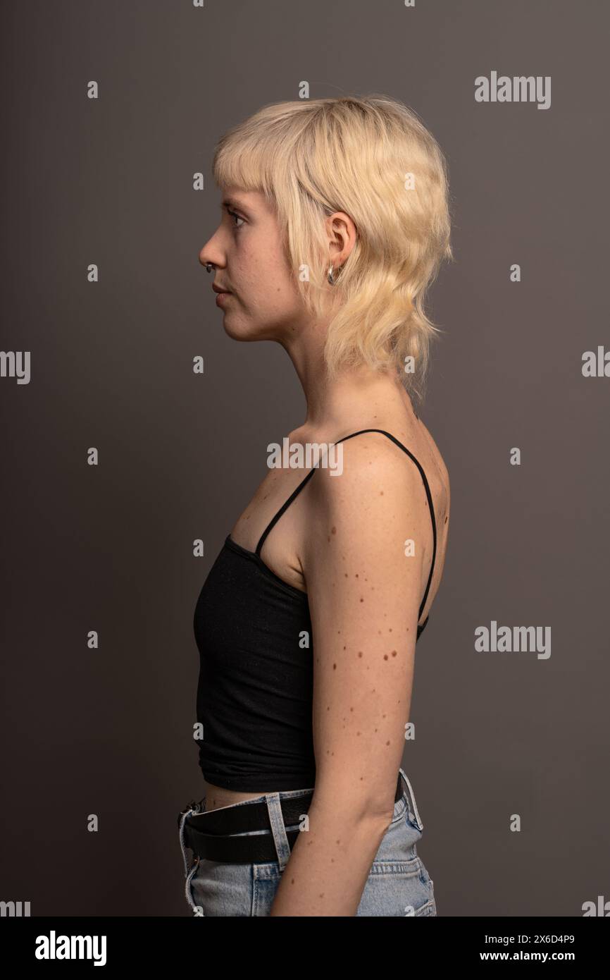 Portrait de profil d'une femme blonde dans un top noir et un Jean, photographie de studio mettant en valeur la mode et le style personnel, fond neutre. Banque D'Images