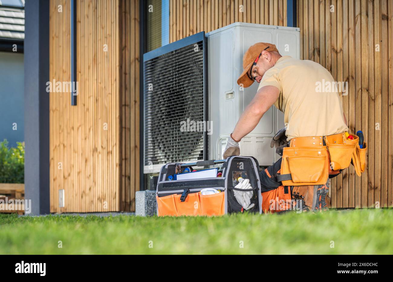 Ouvrier HVAC travaillant sur une pompe à chaleur moderne à l'extérieur d'une maison. Banque D'Images