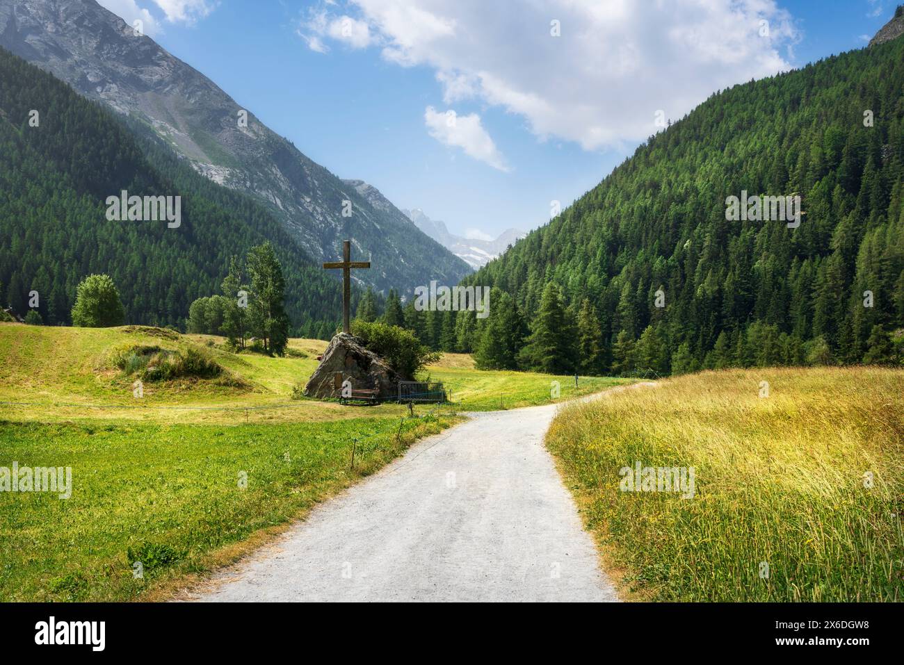 Sentier de montagne et croix chrétienne à Prati di Sant'Orso. Massif du Gran Paradiso en arrière-plan. Cogne, Vallée d'Aoste, Italie Banque D'Images