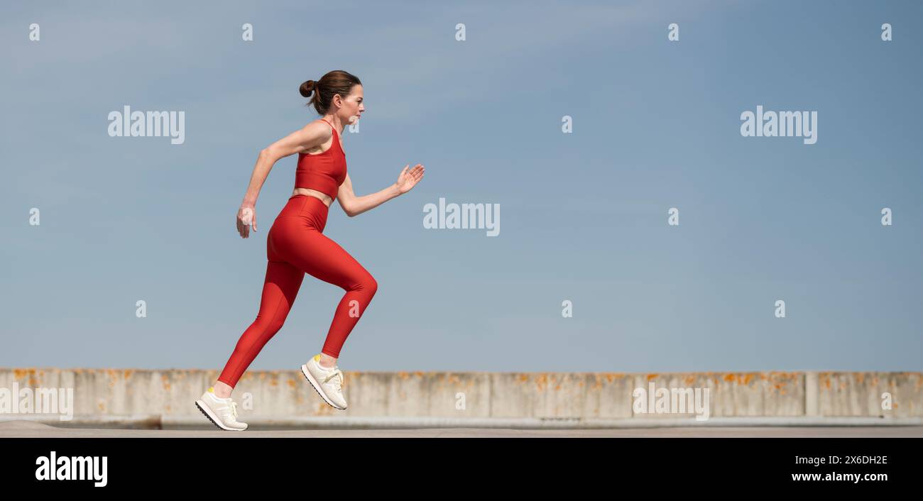 femme adulte moyenne courant et jogging à l'extérieur, fond de ciel bleu Banque D'Images
