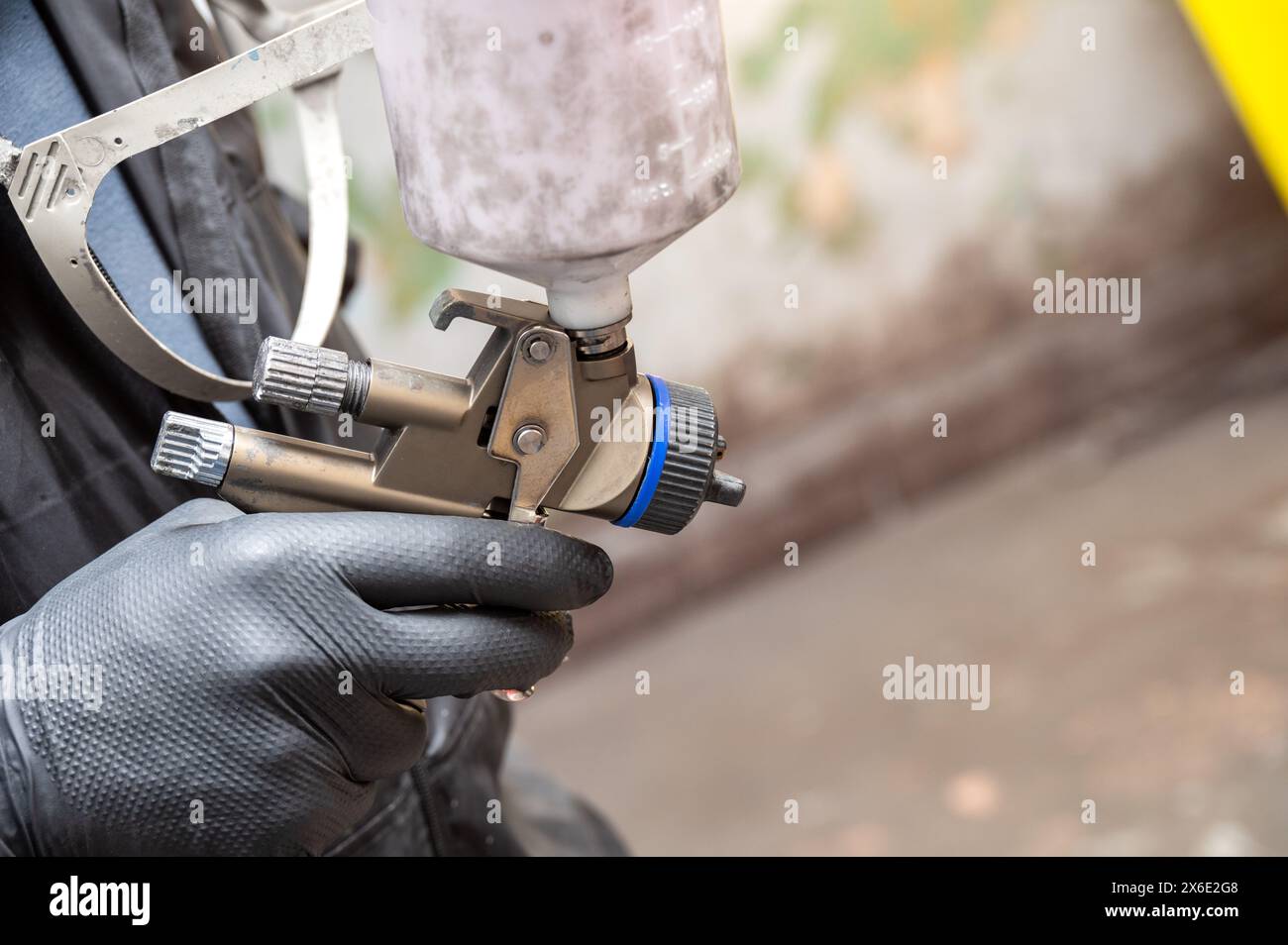 Gros plan de la main d'un peintre professionnel tenant un pistolet de pulvérisation avec un récipient de peinture, prêt pour le travail de carrosserie automobile Banque D'Images