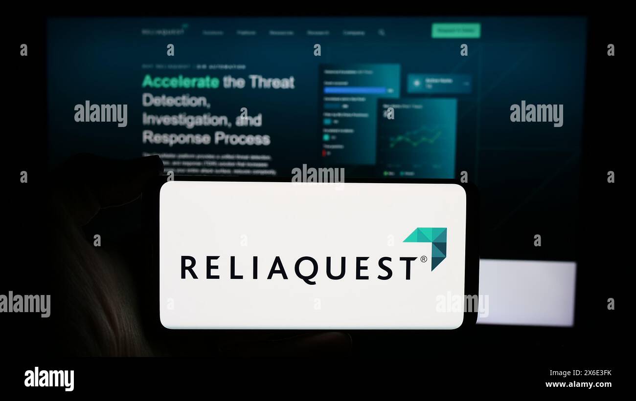 Personne tenant un téléphone portable avec le logo de la société américaine de cybersécurité ReliaQuest LLC en face de la page Web de l'entreprise. Concentrez-vous sur l'affichage du téléphone. Banque D'Images